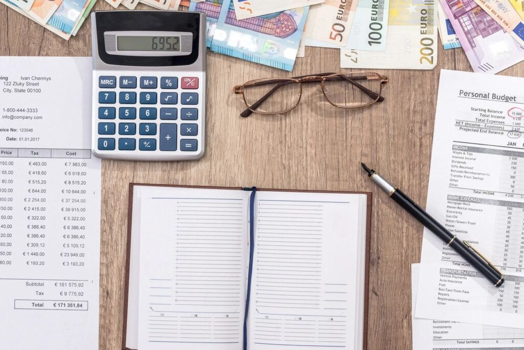 a calculator, notebook, money bills, eyeglasses, pen, and personal budget files